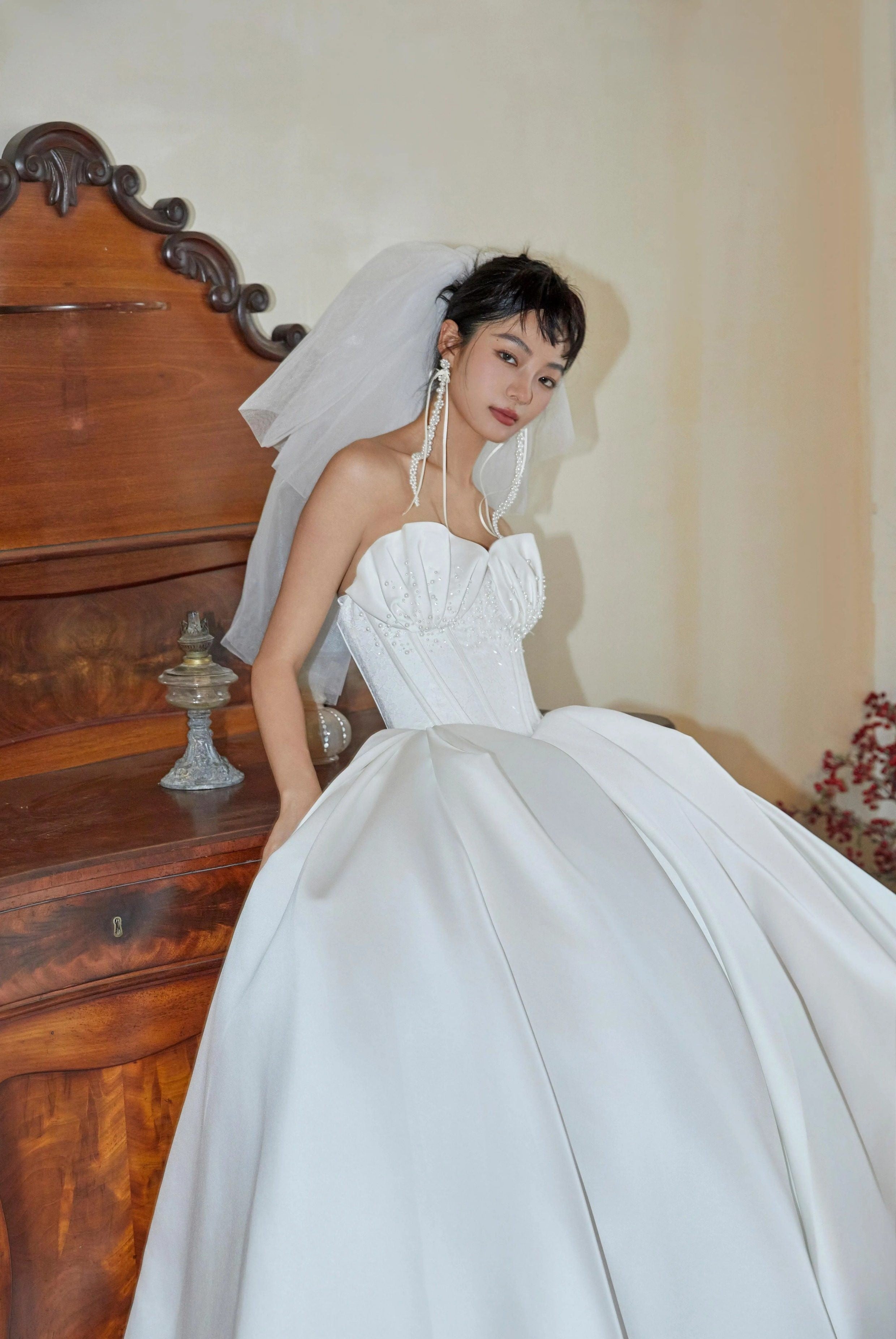 Woman in a white wedding dress with a veil standing in front of a wooden piano.