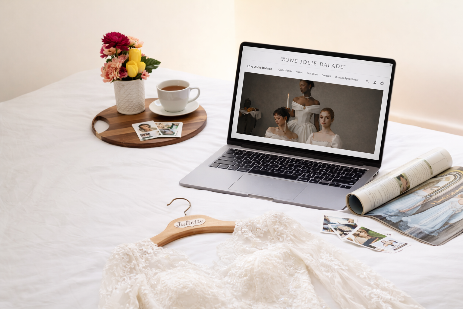 Laptop on a bed with wedding dress, flowers, and tea